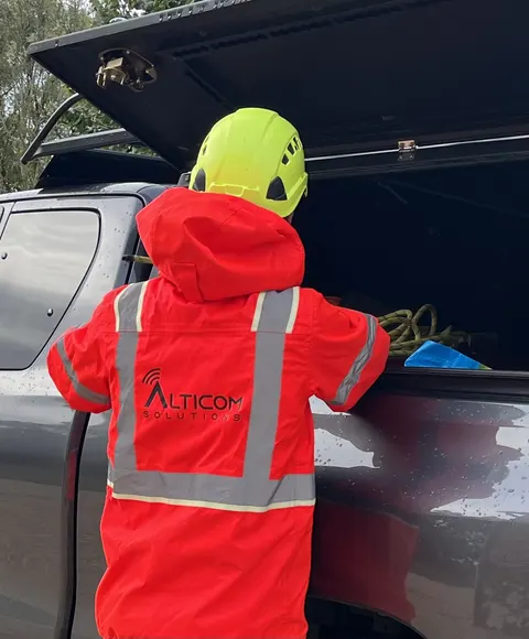 Technicien ALTICOM SOLUTIONS de dos, casque et veste haute visibilité, devant le pick-up de l'équipe